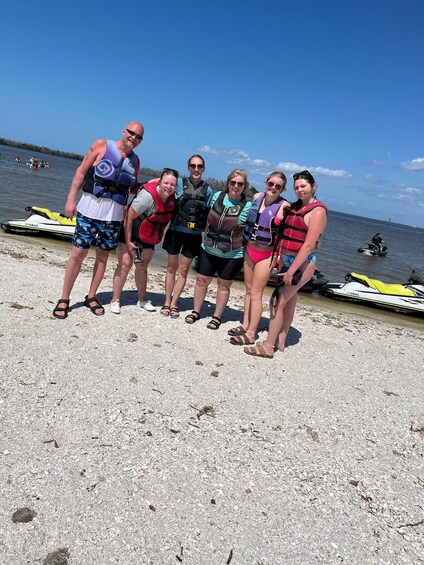 A group of people on a beach with jet skis and a boat in the background. 1