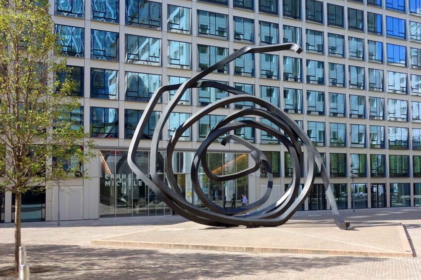 Une sculpture moderne se dresse devant un bâtiment en verre, sur lequel on peut lire l’inscription « CARRE MICHELLE ». 3