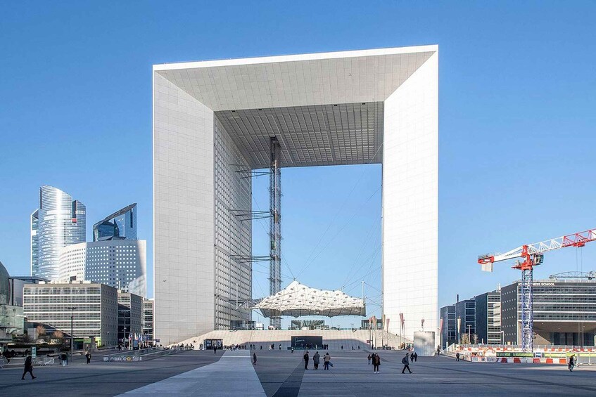 Un grand bâtiment moderne, doté d’une arche imposante, entouré d’autres immeubles de grande hauteur et de grues de construction. 1