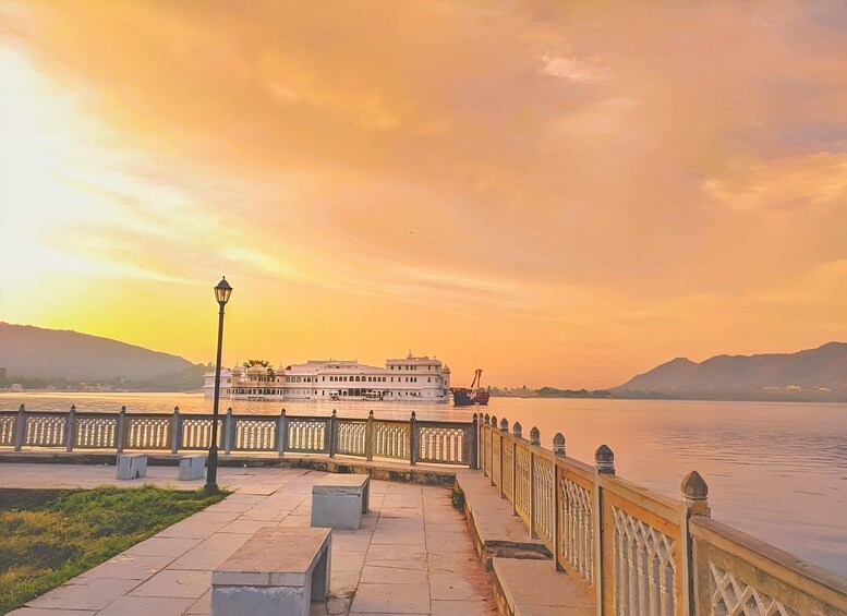 A riverside walkway with a white building and a boat in the background. 4