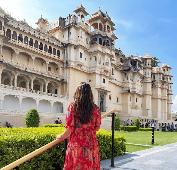 A historic building with ornate architecture, a well-maintained garden, and a person in a red dress. 3