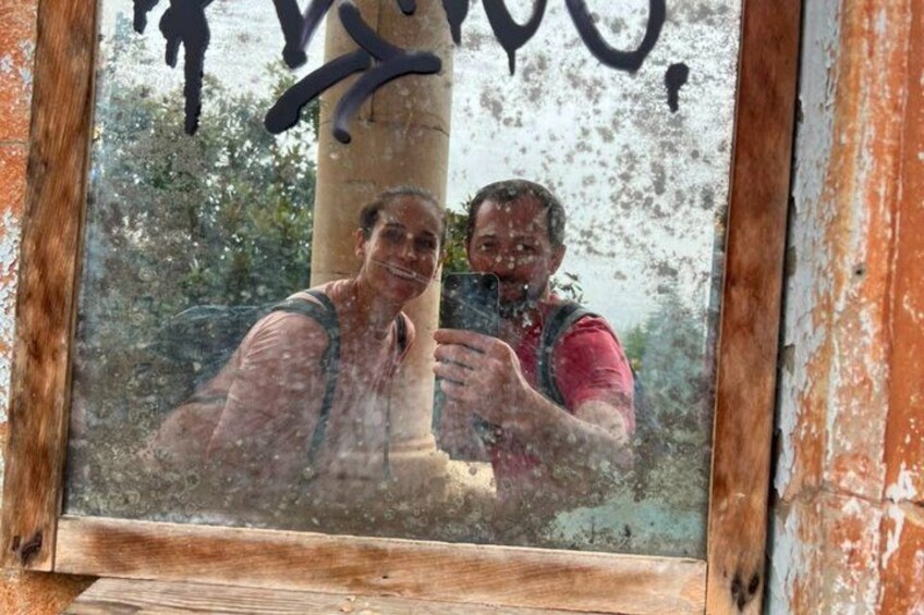A window with a reflection of two people, a wooden frame, and a tree. 3