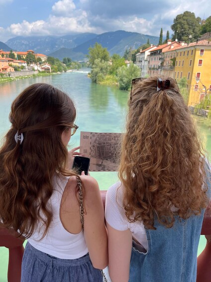 Two people looking at a map, overlooking a river with buildings and mountains in the background. 1