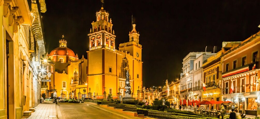 Un edificio histórico con una cúpula y torres, una calle empedrada y zonas de estar al aire libre. 5