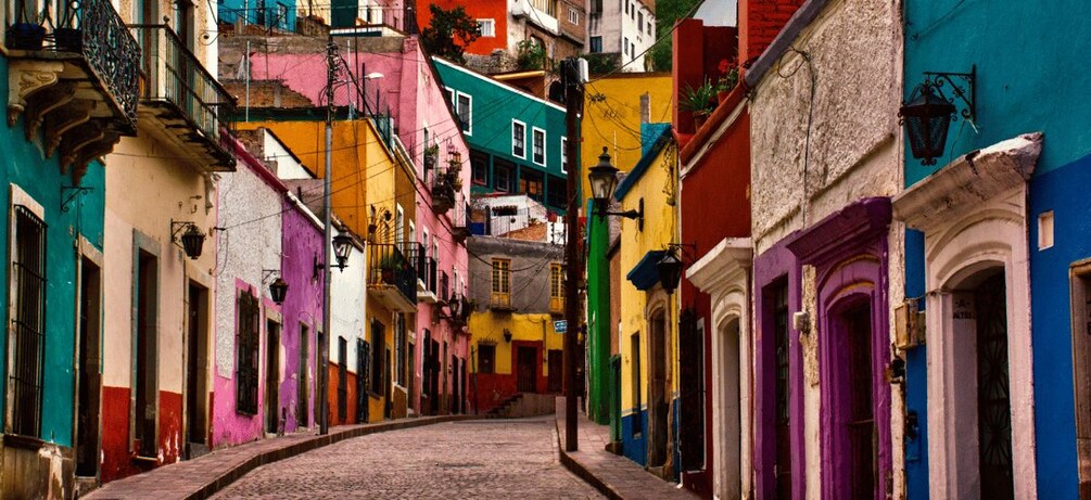 Una estrecha calle adoquinada flanqueada por edificios coloridos, balcones y barandillas de hierro forjado. 4