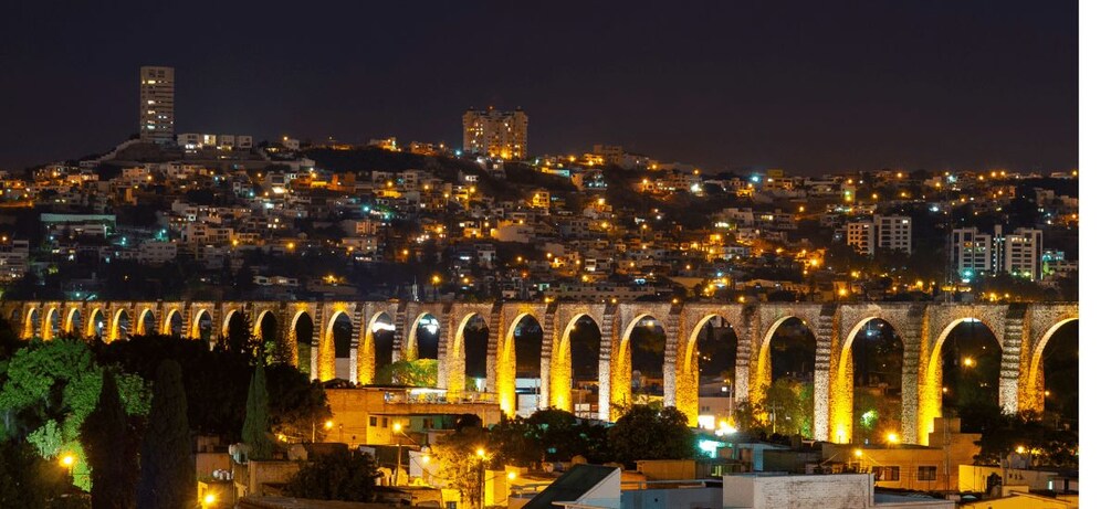 Un paisaje urbano nocturno con una serie de arcos iluminados y un edificio destacado en una colina. 3