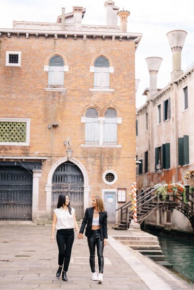 Two women walking on a cobblestone street in front of a historic brick building with arched windows and a canal. 5