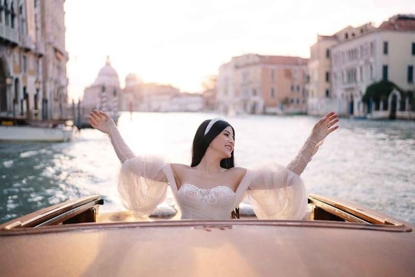 A person in a boat with arms outstretched, surrounded by a canal with buildings on either side. 3