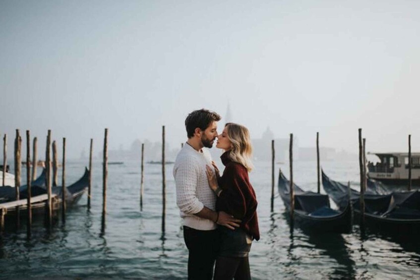 A couple embracing by a waterfront with boats and a hazy cityscape in the background. 2