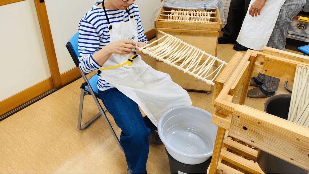 A person in a striped shirt and apron working with wooden sticks, possibly crafting or assembling something. 3