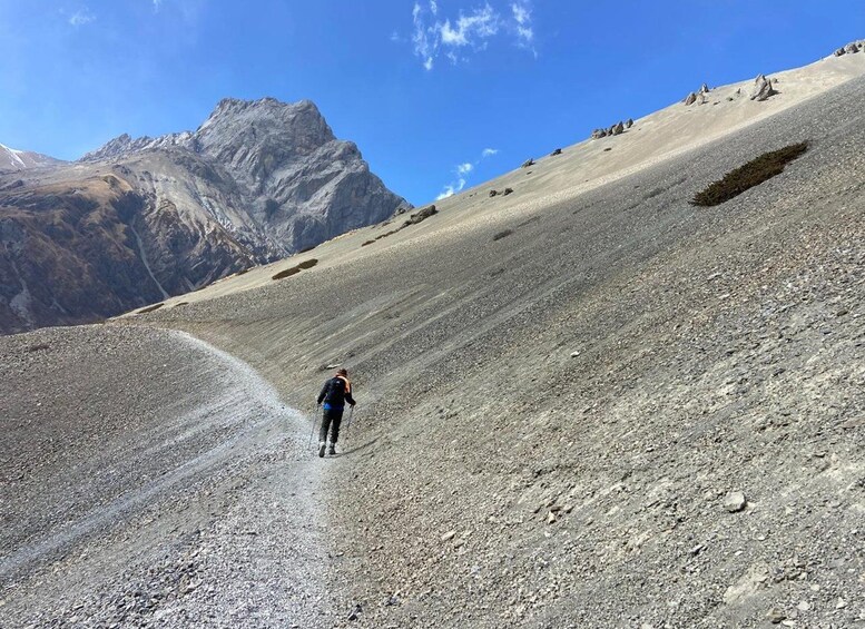 Una persona camina por un sendero pedregoso en la montaña con un gran pico montañoso al fondo. 4