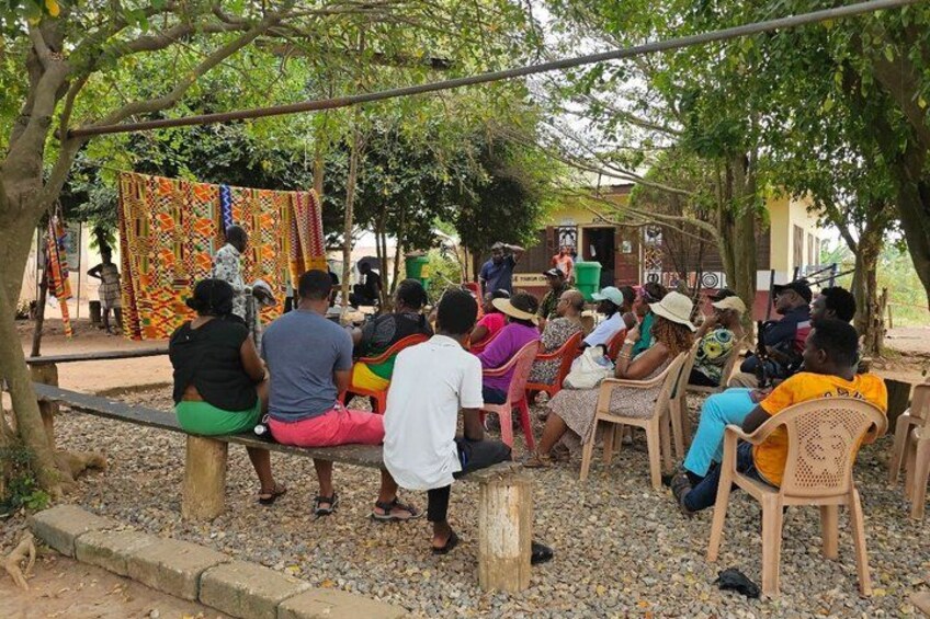 A group of people sitting on benches under trees, with colorful fabrics hanging in the background. 5
