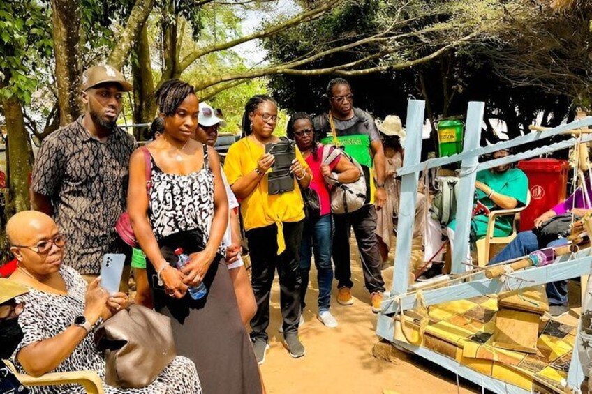 A group of people standing outdoors, some holding phones, with a makeshift structure and bags in the background. 1