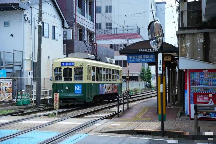 A green and yellow tram at a station with a vending machine and a building in the background. 4