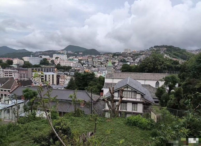 A cityscape with a mix of modern and traditional buildings, a prominent church with a green spire, and mountains in the background under a cloudy sky. 3