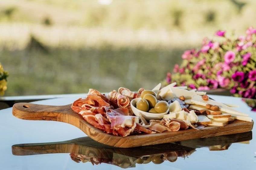 A wooden board with various cheeses, cured meats, and olives. 2