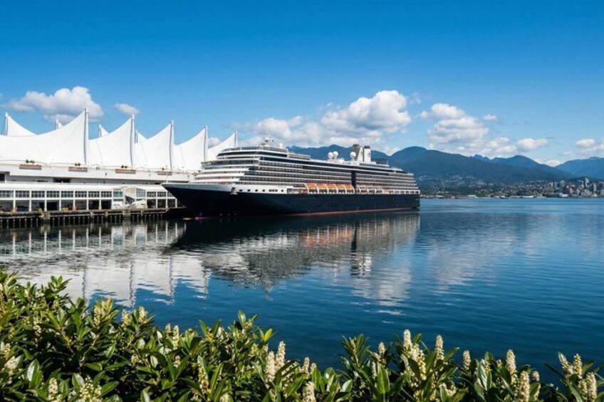 A large cruise ship docked at a port with a white building and mountains in the background. 2