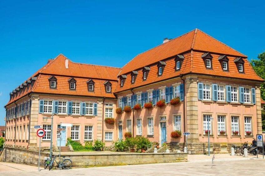 A historic building with a red-tiled roof and blue shutters, a bicycle parked in front, and a no parking sign. 2