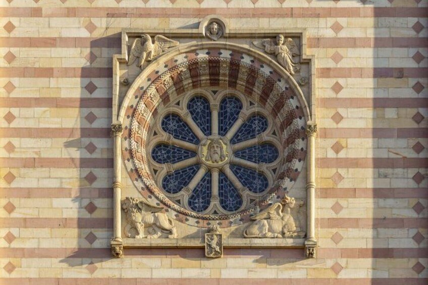 A stained glass window with a circular design, flanked by two lions, set in a brick wall with diamond patterns. 3