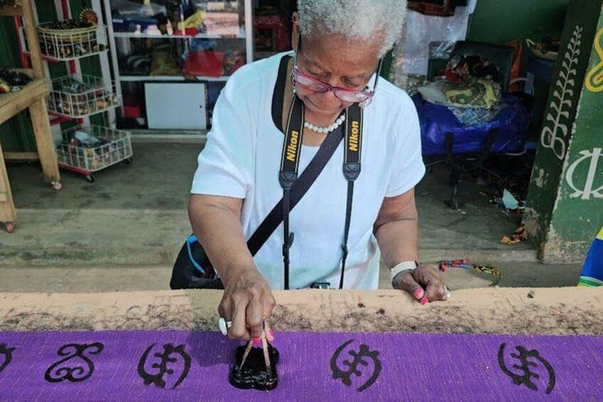 A person painting a purple cloth with black symbols. 1