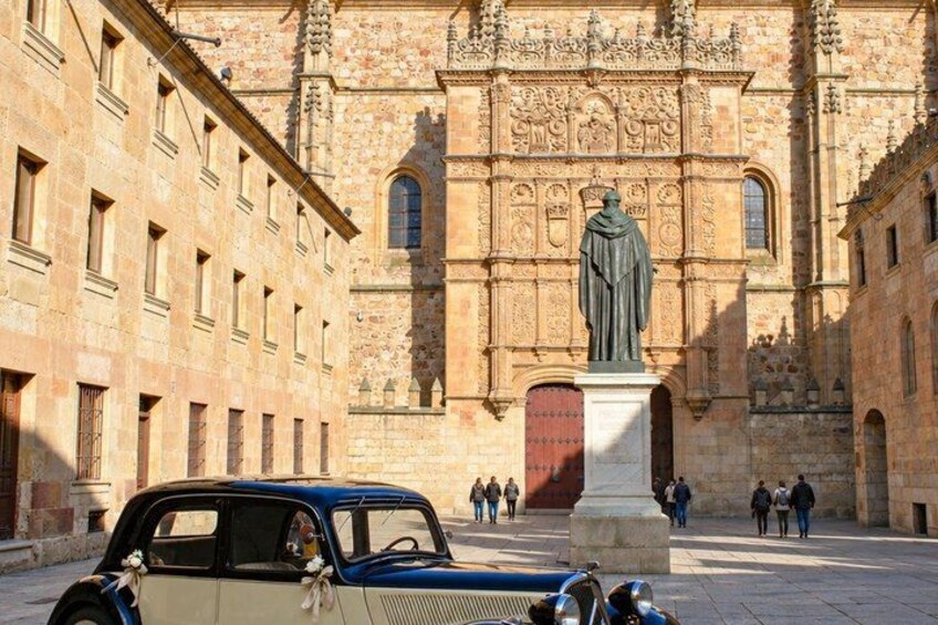 A historic building with a statue, a vintage car, and people walking in the foreground. 3