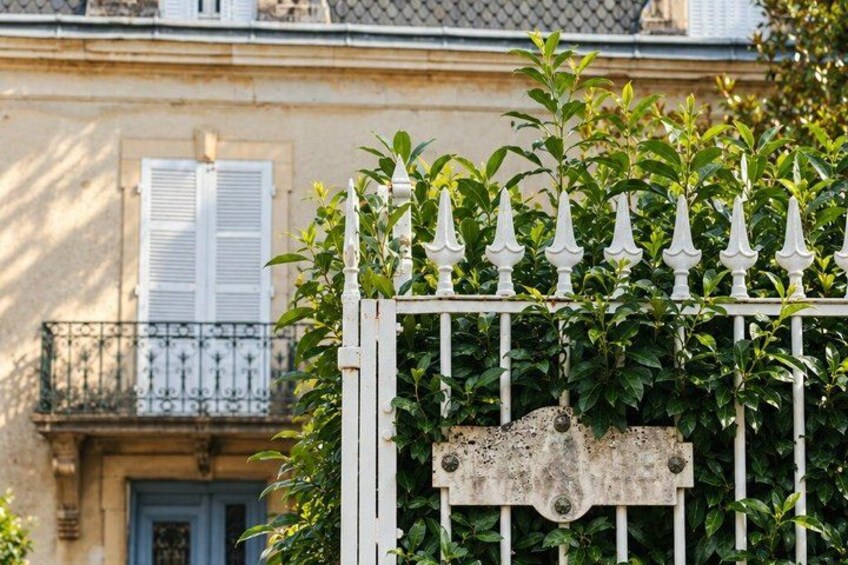 A white metal gate with greenery, a balcony with white shutters, and a building facade. 5