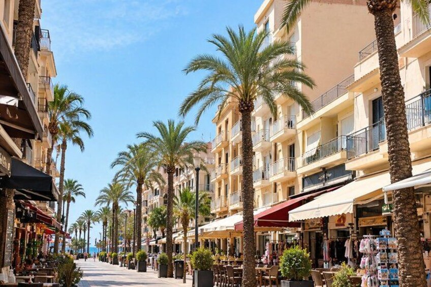 A sunny street lined with palm trees and multi-story buildings with balconies. 3