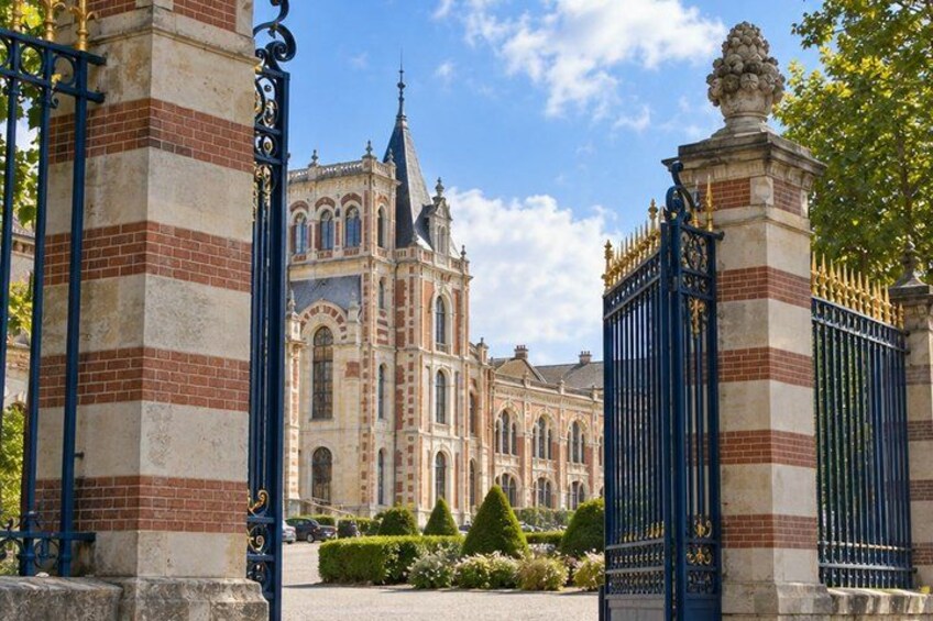 A historic building with ornate architecture, a gated entrance, and well-maintained gardens. 1