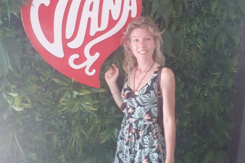 A person standing in front of a Coca-Cola sign with a green leafy background. 5