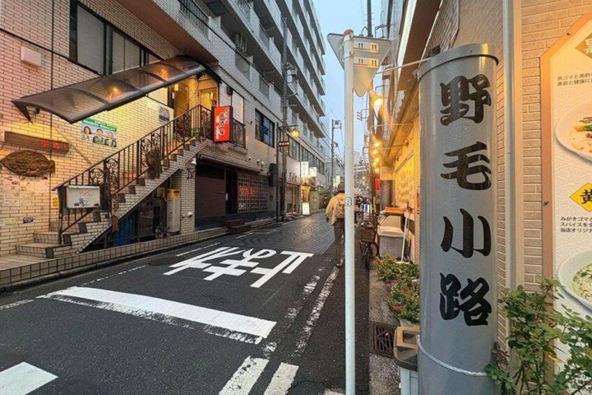 A street with a crosswalk, a building with a sign, and a pole with text. 5