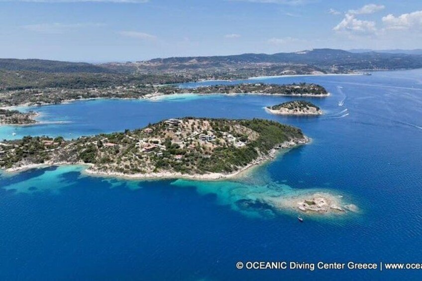 An aerial view of a coastal area with multiple islands, clear blue waters, and a hilly landscape. 1