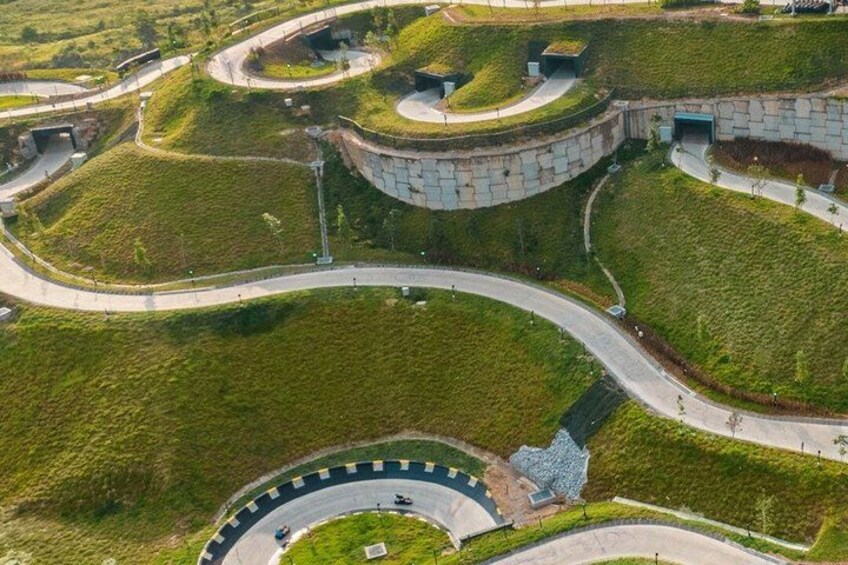 A circular building with a green roof, surrounded by grassy areas and winding roads. 5