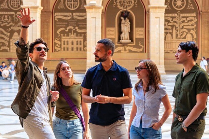 A group of people in an outdoor area with classical architecture, including columns and detailed wall carvings. 5