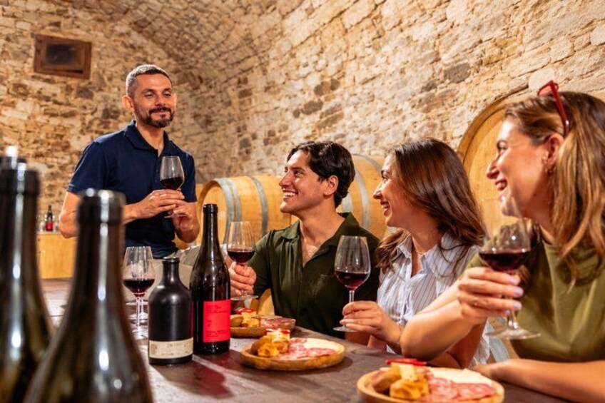 A group of people tasting wine in a cellar with barrels in the background. 1