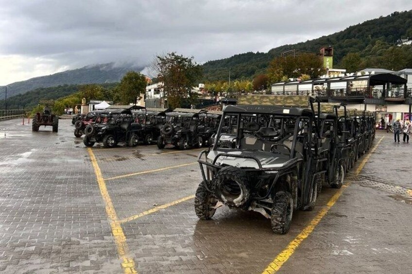 A row of off-road vehicles parked in a lot with a mountainous backdrop. 5