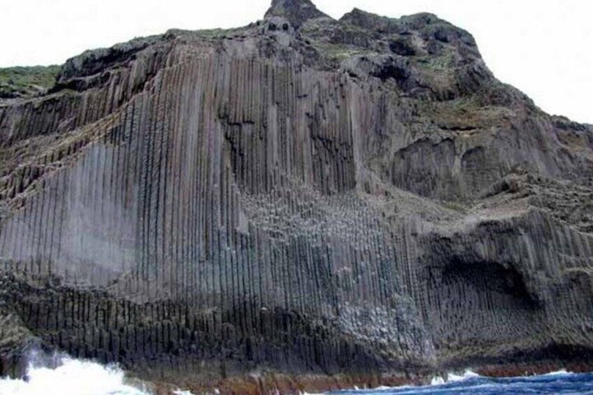 A rugged cliff with vertical striations and a cave entrance. 2
