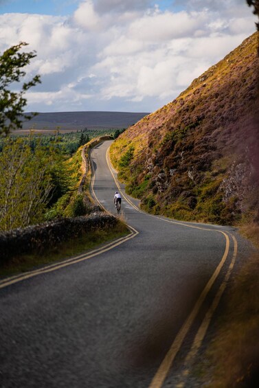 A cyclist on a winding road surrounded by hills and vegetation. 3