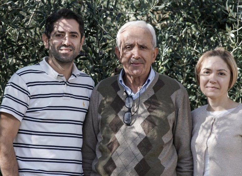Three people standing in front of a dense olive tree. 3