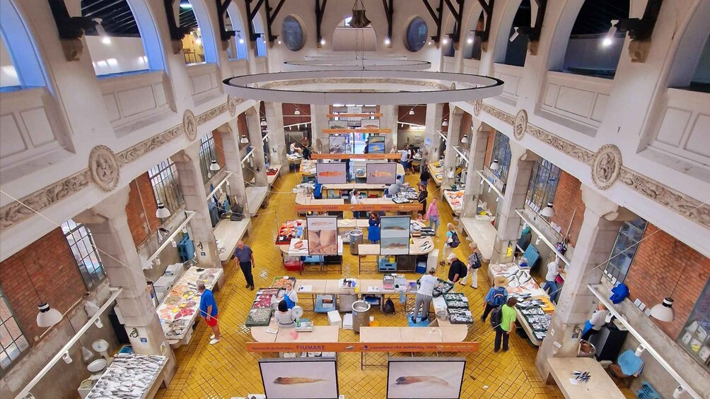 An indoor market with multiple stalls selling various goods, surrounded by high ceilings and decorative columns. 3