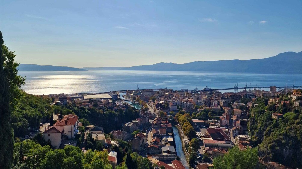 A coastal cityscape with a river, buildings, and mountains in the background. 1