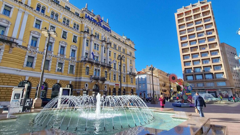 A city square with a fountain, yellow buildings, and a tall residential building. 5
