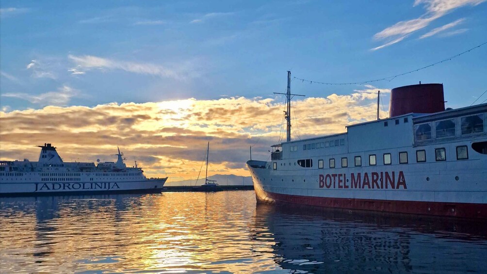 Two boats, one named 'JADROLINJA' and the other 'BOTTELMARINA', docked at a harbor with a sunset sky. 4