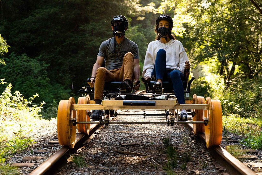 Deux personnes se déplacent à bord d’un chariot en bois sur des voies ferrées, entourées de verdure. 3