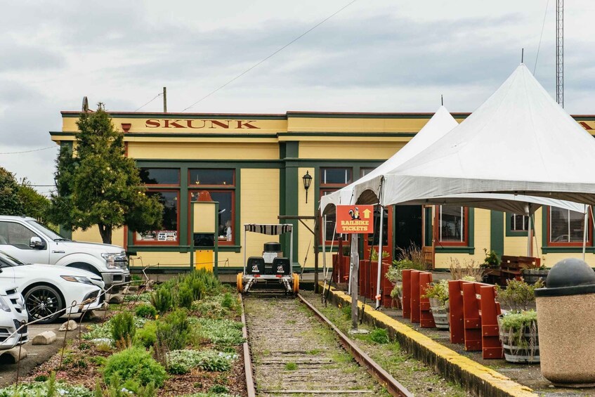 Une gare avec un bâtiment portant l’inscription « SKUNK », un petit train sur les rails et une tente blanche. 2