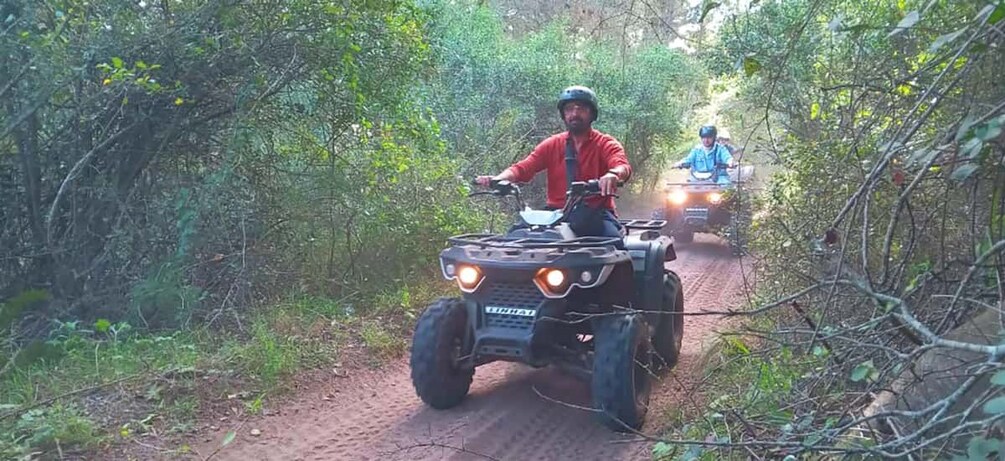 Deux personnes conduisent des quads sur un chemin de terre, entourés d’une forêt dense. 5