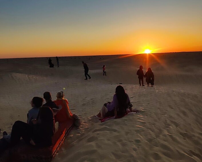 Un groupe de personnes assises et debout sur une plage de sable au coucher du soleil. 3