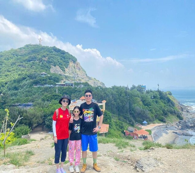 Una familia en la montaña, con vista al océano y una estatua al fondo. 5