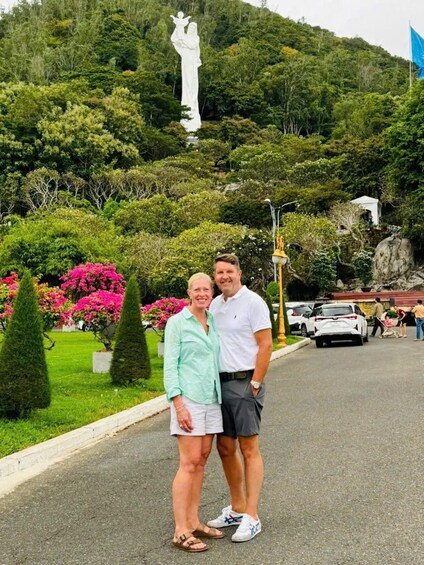 Dos personas en un parque, con una estatua al fondo y una bandera azul en un asta. 3