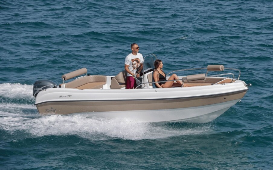 Un bateau à moteur avec deux personnes à bord, l’une debout et l’autre assise, navigue sur des eaux calmes et bleues. 1