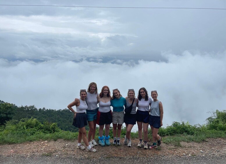Un groupe de personnes se tient sur un chemin de terre, avec un ciel nuageux et des collines boisées en arrière-plan. 5
